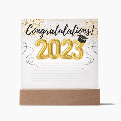 A sentimental plaque with heartfelt message, that begins with congratulations 2023, sitting on top of an illuminated base, placed on a desk.