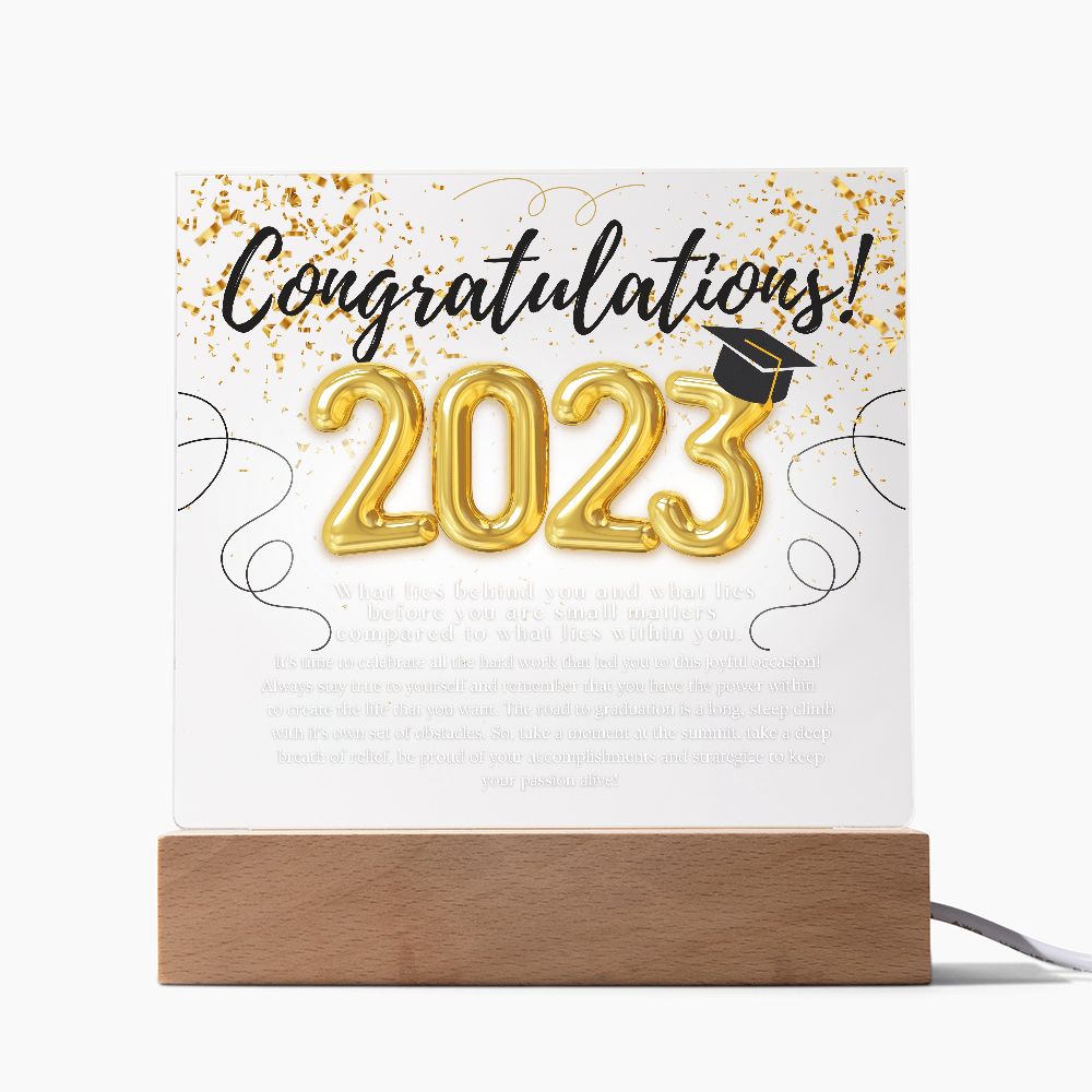 A sentimental plaque with heartfelt message, that begins with congratulations 2023, sitting on top of an illuminated base, placed on a desk.